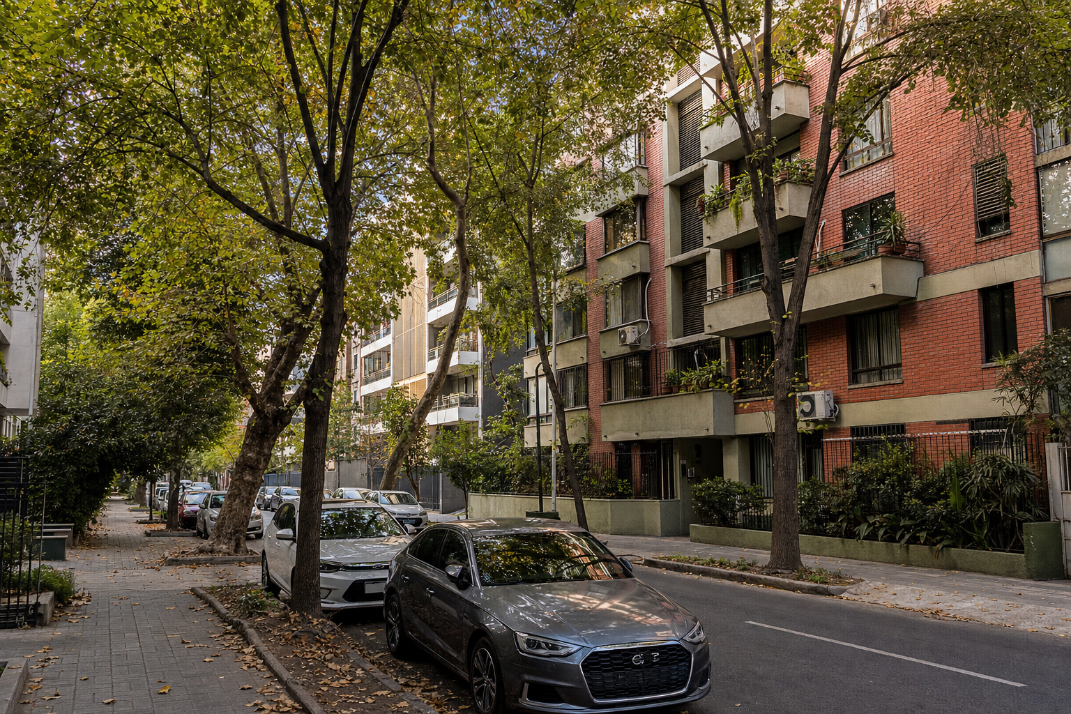Calle arbolada de Ñuñoa con edificios de departamentos y autos estacionados