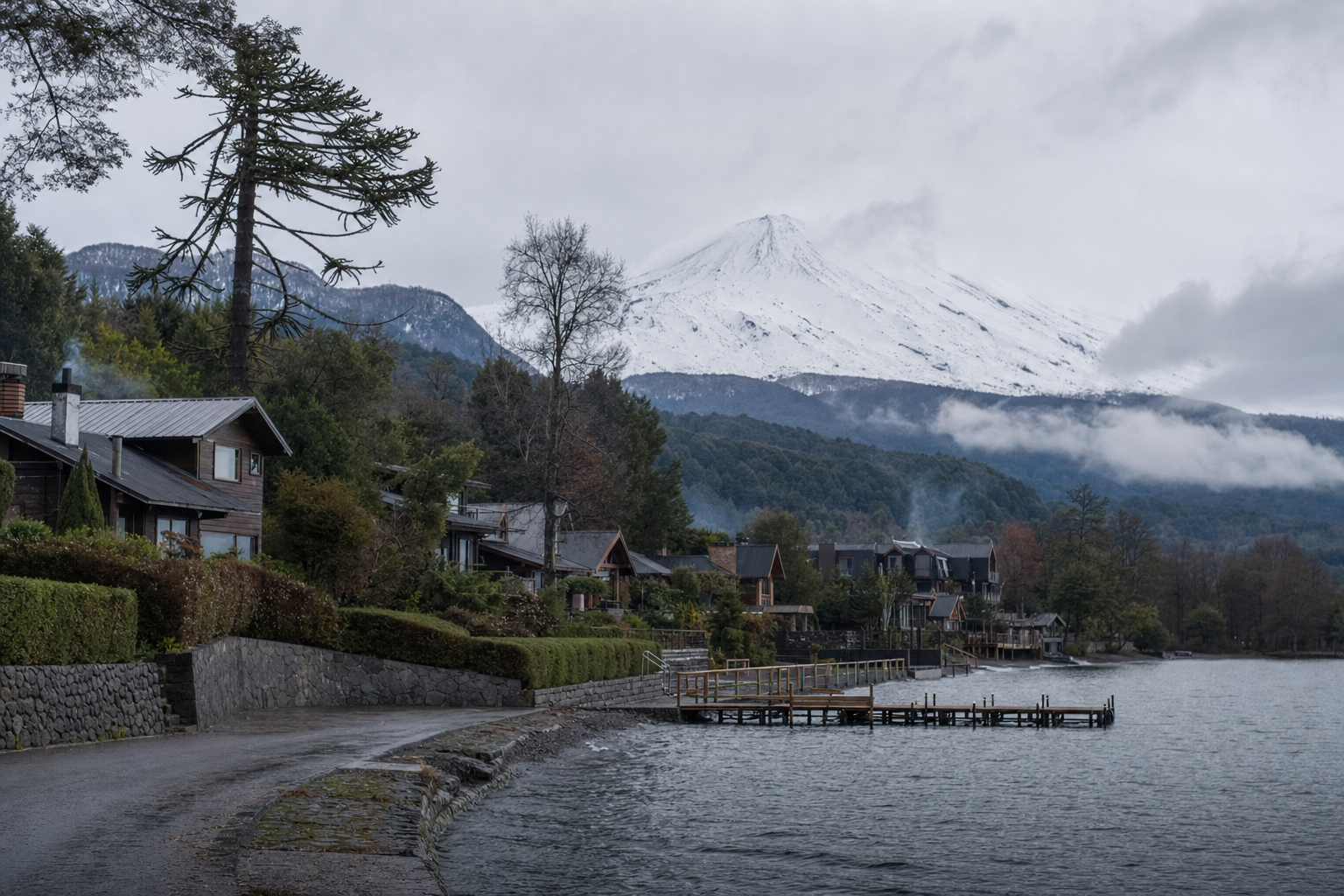 Casas y cabañas a orillas del lago Villarrica con el volcán nevado entre nubes